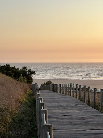 Wooden boardwalk leading to a calm ocean beach at sunset