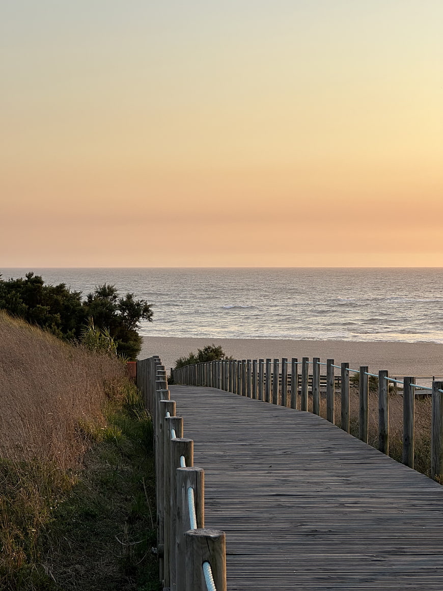 Wooden boardwalk leading to a calm ocean beach at sunset