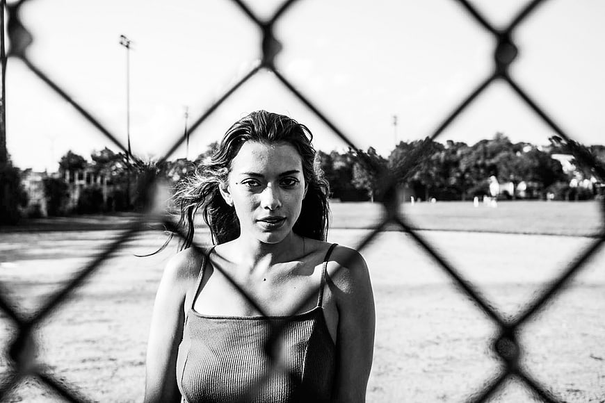 Black and white portrait of young woman behind chain link fence
