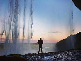 Silhouette of Man Standing Behind Waterfall at Sunset