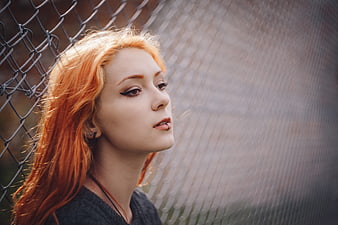 Redhead woman with piercings leaning against chain link fence