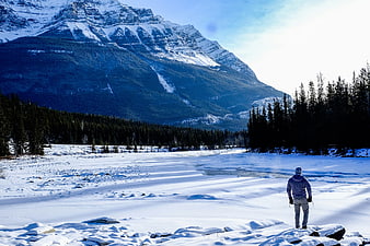 Man standing on frozen river looking at snowy mountain landscape