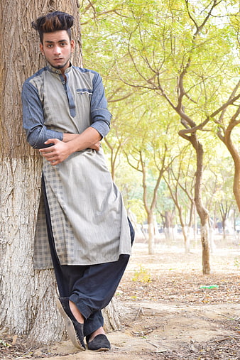 Young man in traditional shalwar kameez leaning against tree