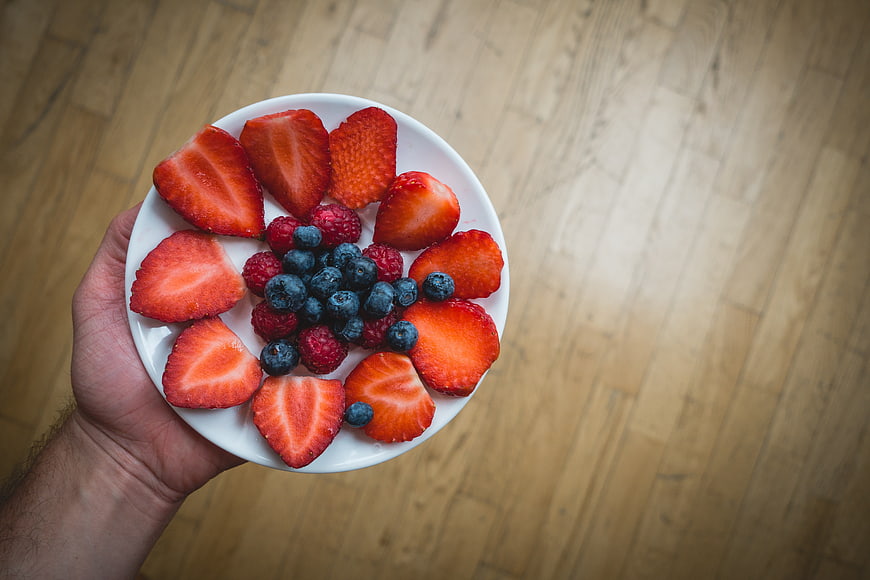 Hand holding plate of fresh strawberries, raspberries, and blueberries