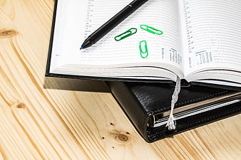 Open planner with black pen and green paperclips on wooden desk