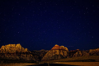 Desert Highway Under Starry Night Sky with Illuminated Mountains