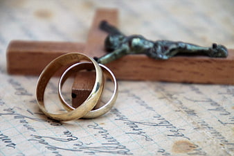 Gold and silver wedding rings with wooden crucifix on old handwritten paper