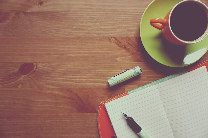 Flat lay of coffee cup, notebook, and pen on wooden table