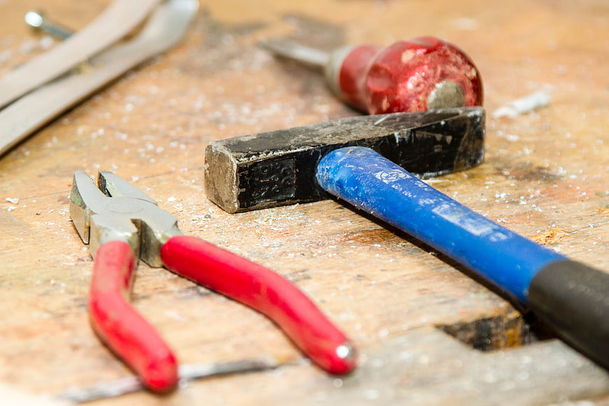 Close-up of used hammer and pliers on wooden workbench