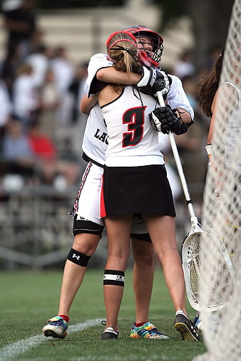 Two female lacrosse players hugging on field
