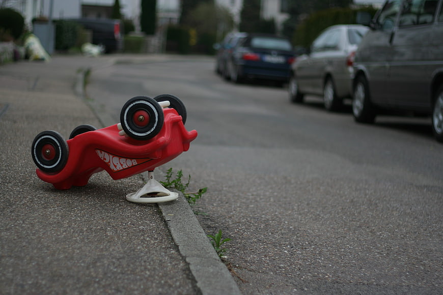 Red toy car overturned on suburban street curb