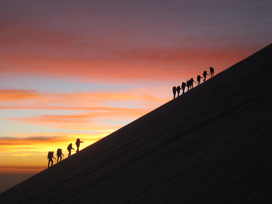 Silhouetted Mountaineers Climbing Slope at Sunrise