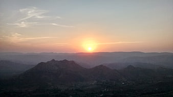 Serene sunset over layered mountain ranges with soft pastel sky