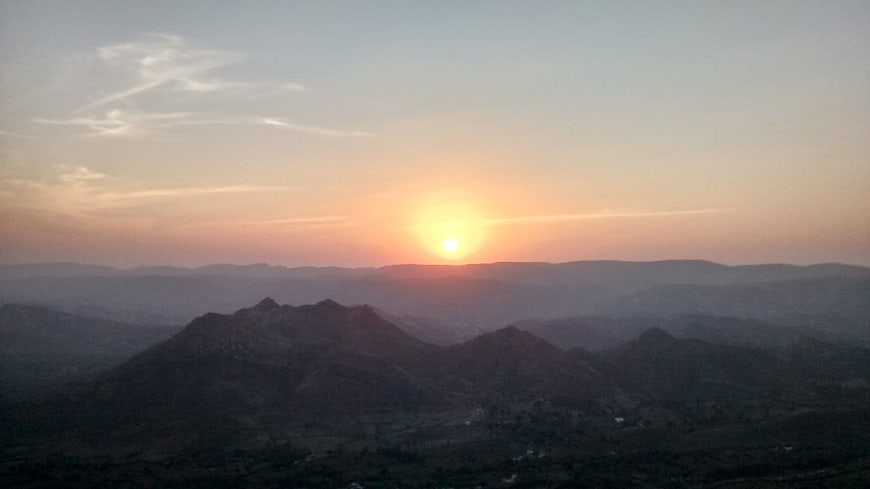 Serene sunset over layered mountain ranges with soft pastel sky