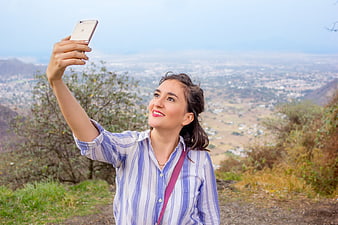 Happy woman taking selfie on mountain overlooking city