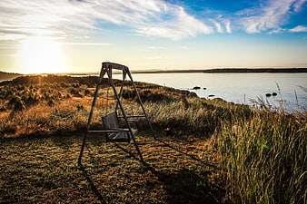 Wooden Swing on Grassy Cliff Overlooking Lake at Sunset