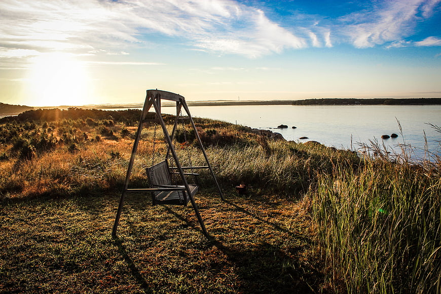 Wooden Swing on Grassy Cliff Overlooking Lake at Sunset