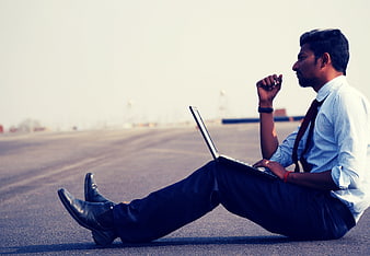 Young Indian businessman working on laptop sitting on road