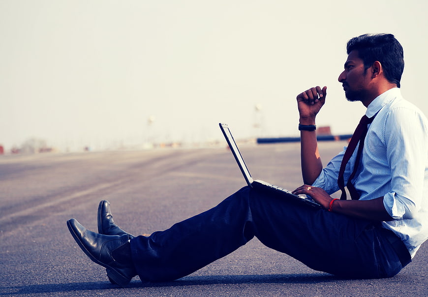 Young Indian businessman working on laptop sitting on road