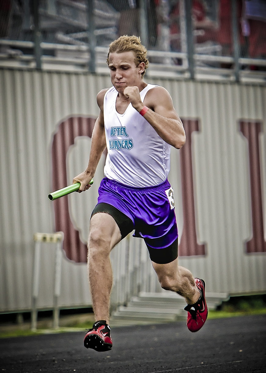 Male Relay Runner Sprinting with Baton on Track