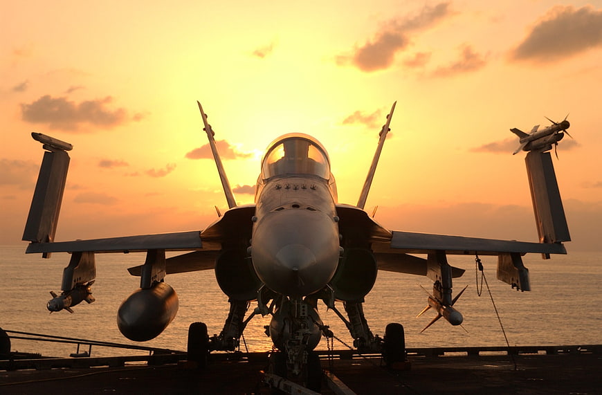 F/A-18 Hornet fighter jet on aircraft carrier deck at sunset