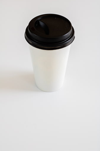 White disposable coffee cup with black lid on white background