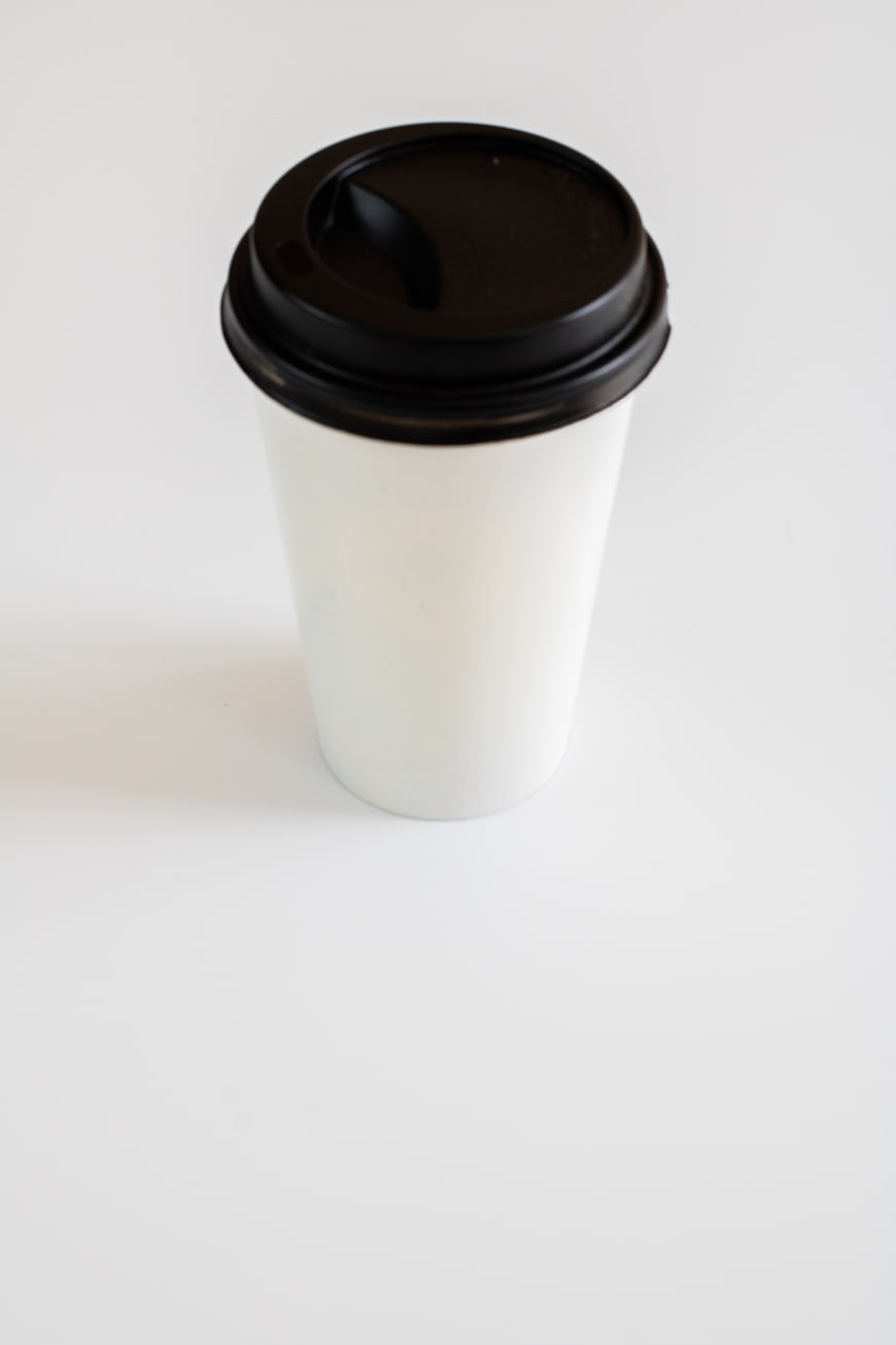 White disposable coffee cup with black lid on white background