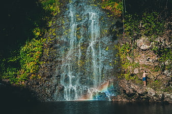 Man climbing cliff near waterfall with rainbow