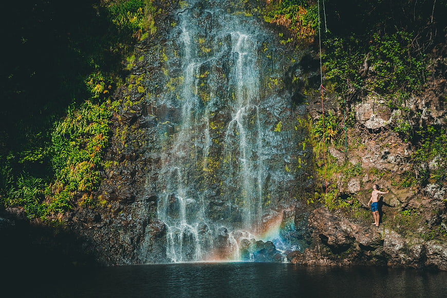 Man climbing cliff near waterfall with rainbow