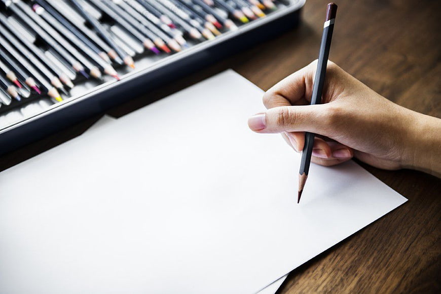 Hand holding colored pencil over blank paper with art set