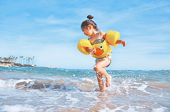 Happy little girl running in ocean waves with yellow duck floaties