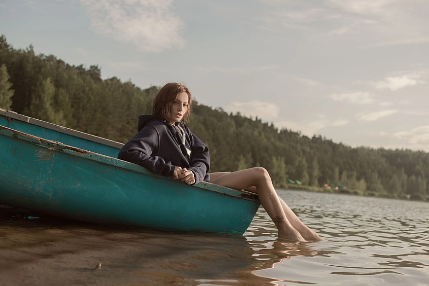 Woman in Hoodie Sitting in Blue Boat by Lake