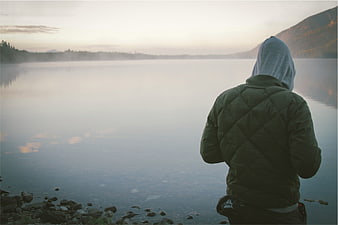 Man in Hoodie Standing by Misty Lake Shore