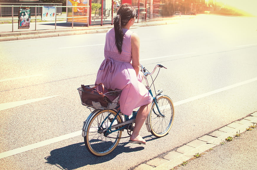 Woman in pink dress riding bicycle on sunny city street