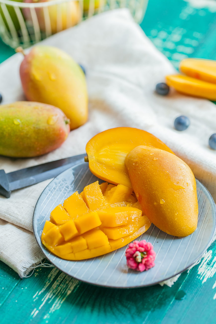 Fresh sliced mangoes on a blue plate with whole fruit