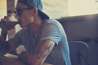 Tattooed Man Drinking From Mason Jar At Cafe