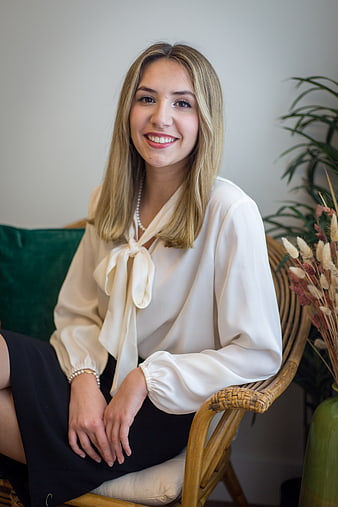 Smiling blonde woman in white blouse sitting in rattan chair