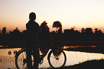 Silhouette of Person with Bicycle at Sunset by Water