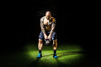 Muscular tattooed man lifting kettlebell in dark gym