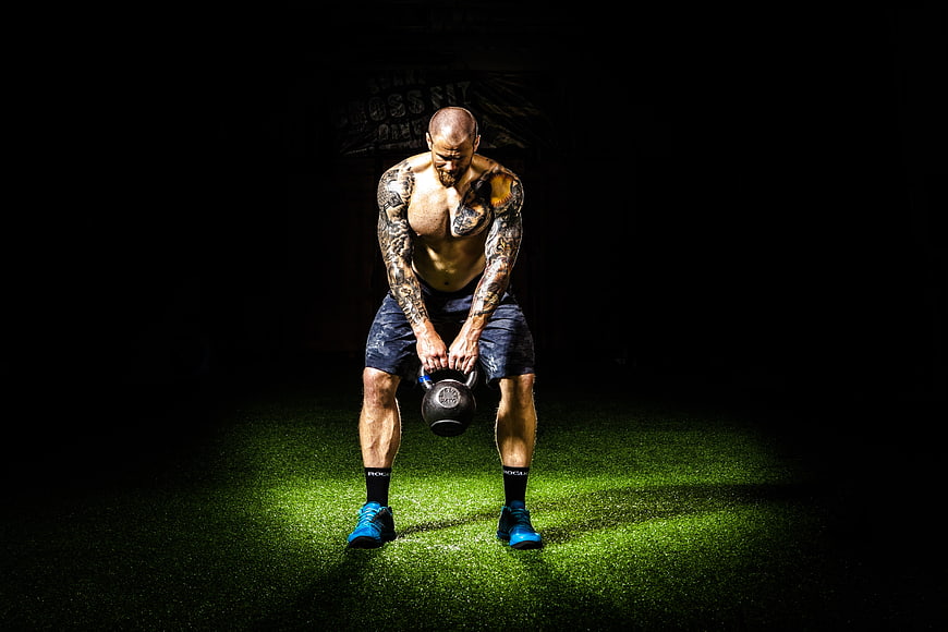 Muscular tattooed man lifting kettlebell in dark gym