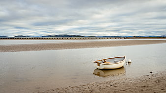 Solitary white rowboat on sandy tidal flat under cloudy sky