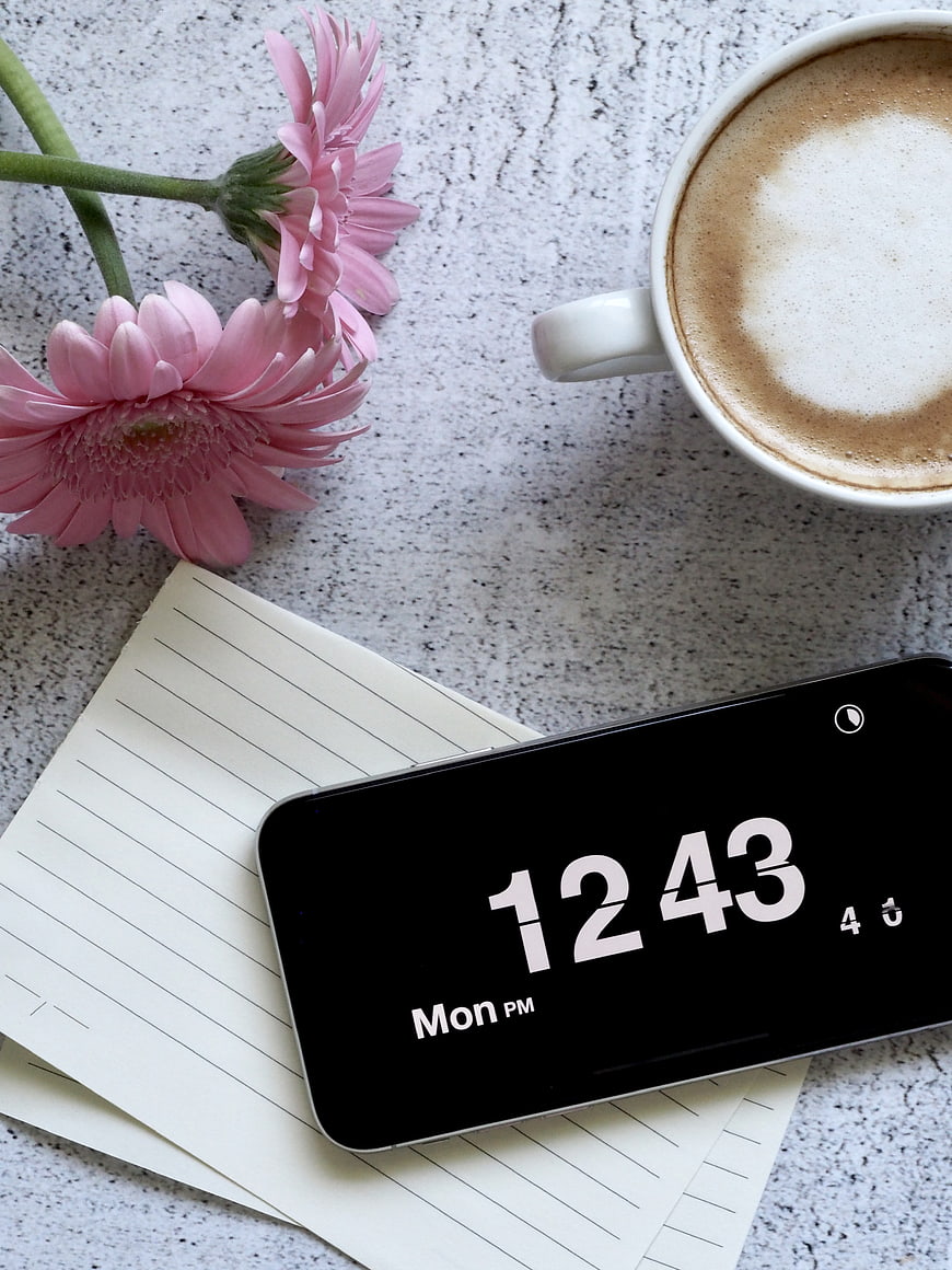 Flat lay of smartphone, coffee, and pink flowers on desk