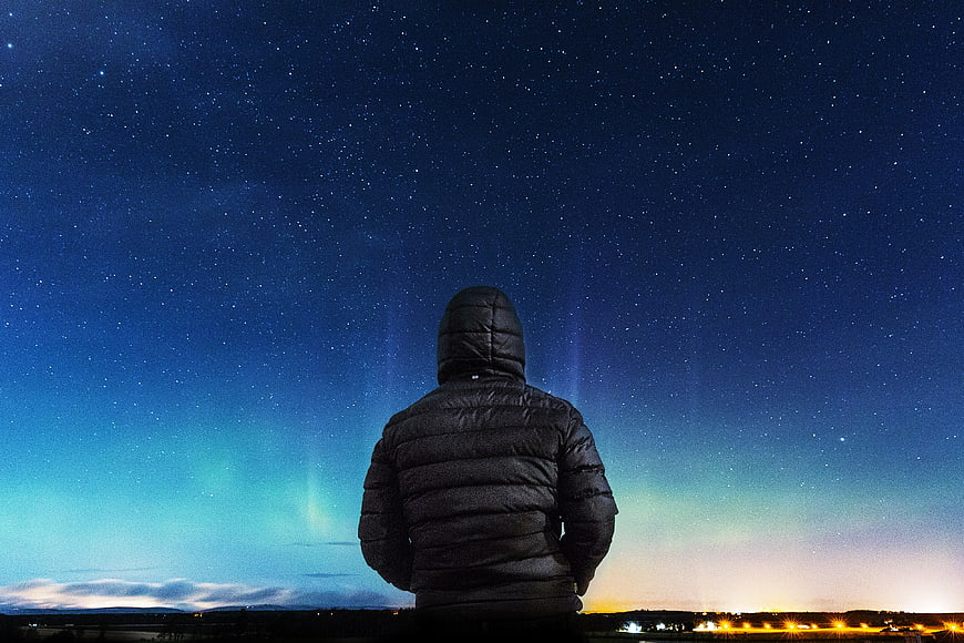 Man in Hoodie Watching Aurora Borealis Under Starry Night Sky