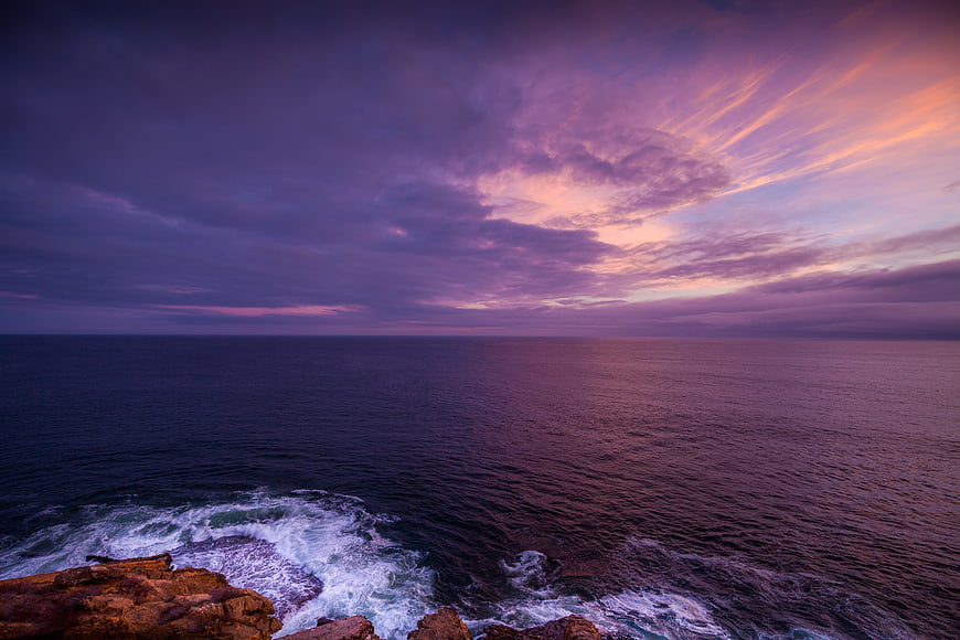 Dramatic Purple Sunset Over Ocean with Rocky Coastline