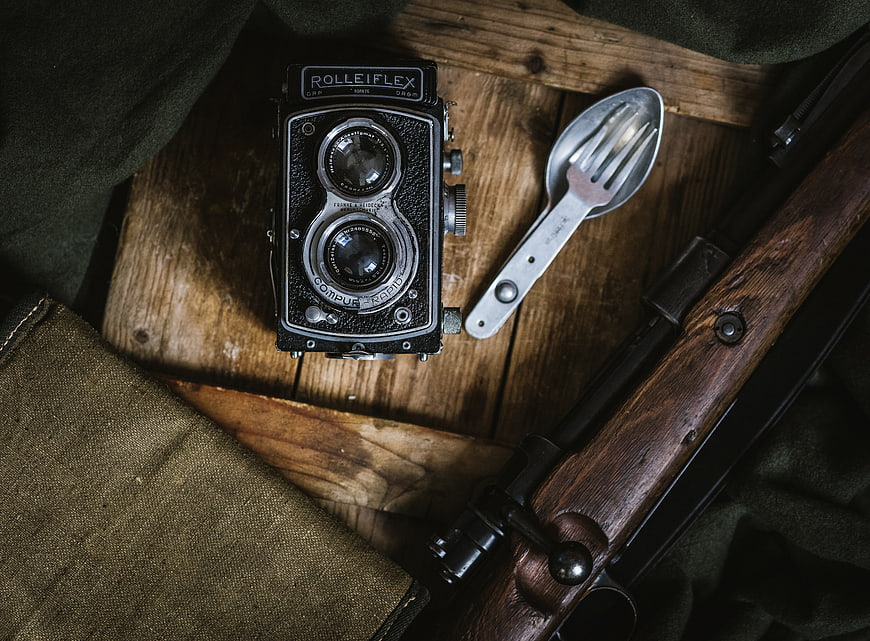 Vintage Rolleiflex Camera, Spork, and Rifle on Wooden Surface