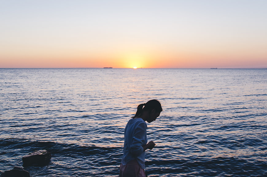 Woman standing by ocean at sunset looking down