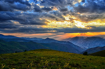 Dramatic Sunset Over Layered Mountain Ranges and Green Meadow