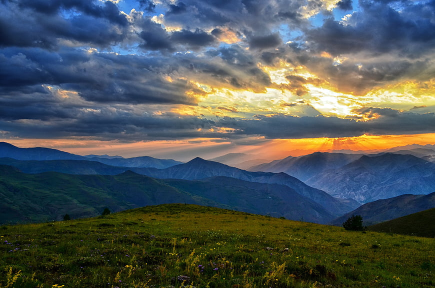 Dramatic Sunset Over Layered Mountain Ranges and Green Meadow