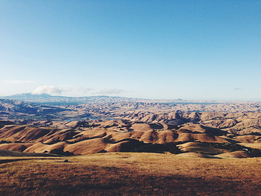 Golden rolling hills landscape with blue sky and distant mountains