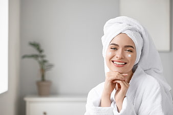 Happy woman with towel on head applying face cream